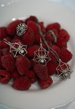 Silver spider web earrings on raspberries on a white plate